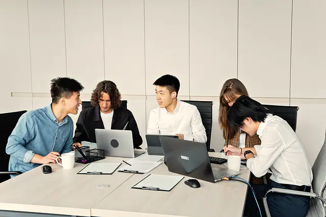 Five people with laptops working together around a meeting table.